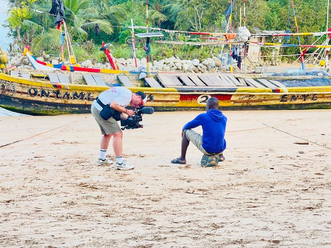Crew filming an interview with a fisherman on the beach beside his canoe in Dixcove